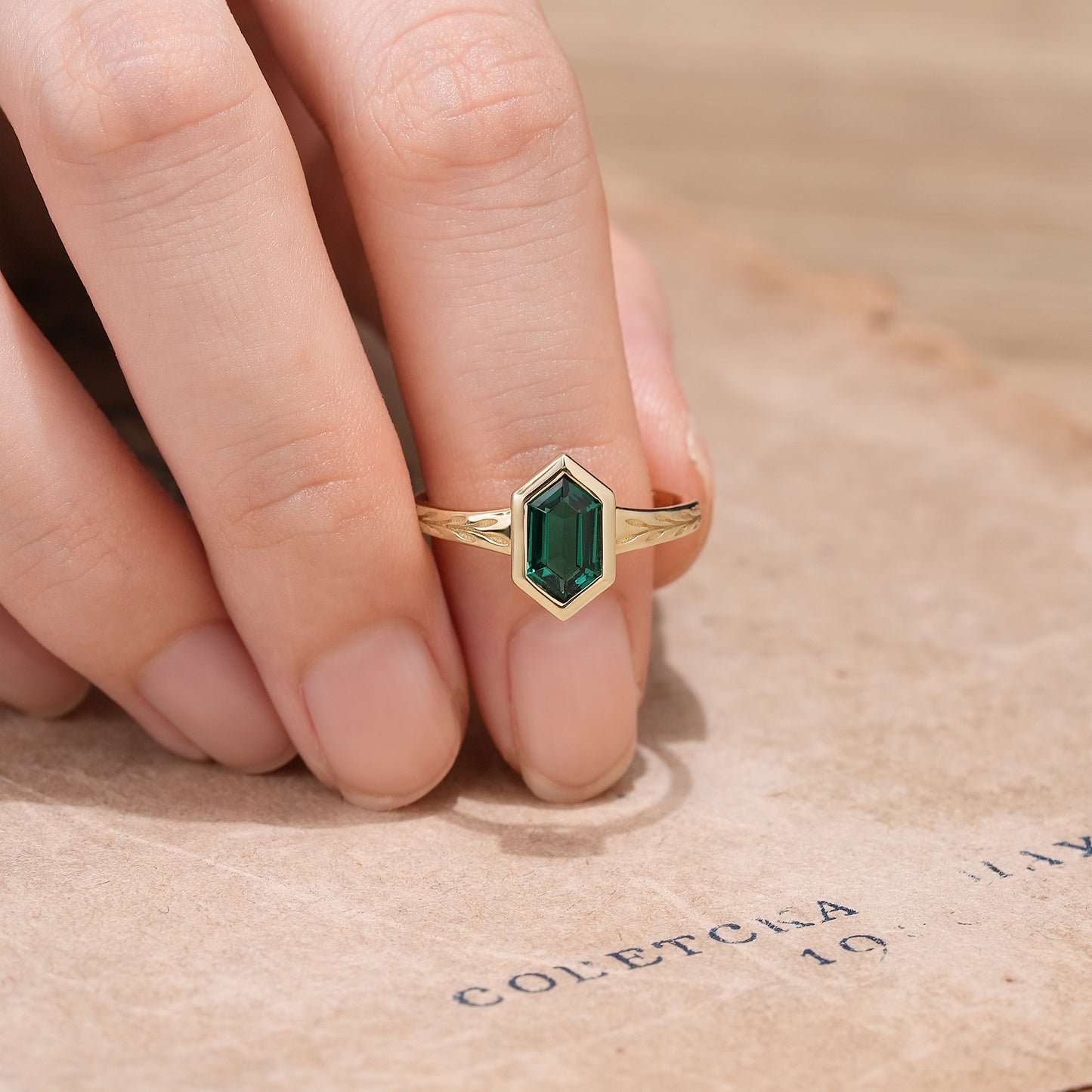 Hand wearing hexagon emerald ring with leaf accents on gold band