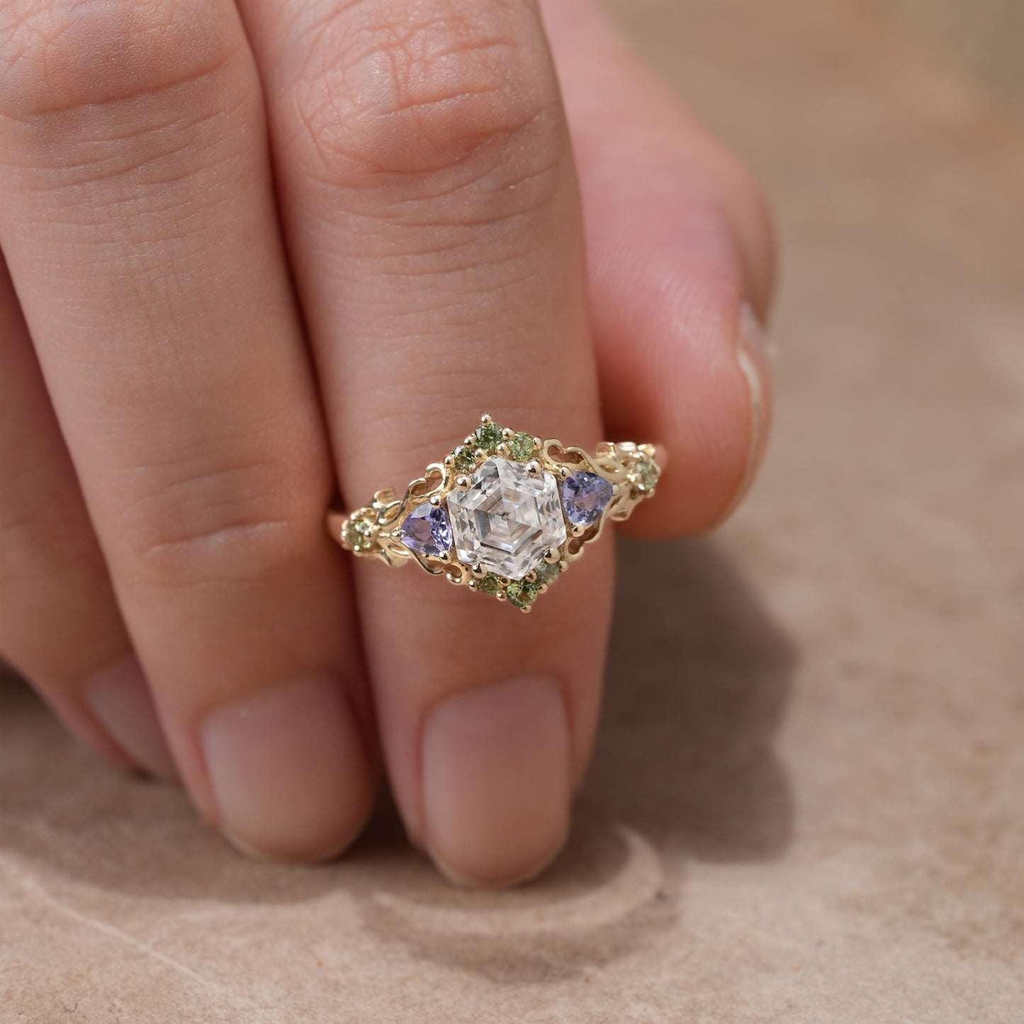 Moissanite leaf ring with tanzanite and green sapphire, set in gold, on hand.