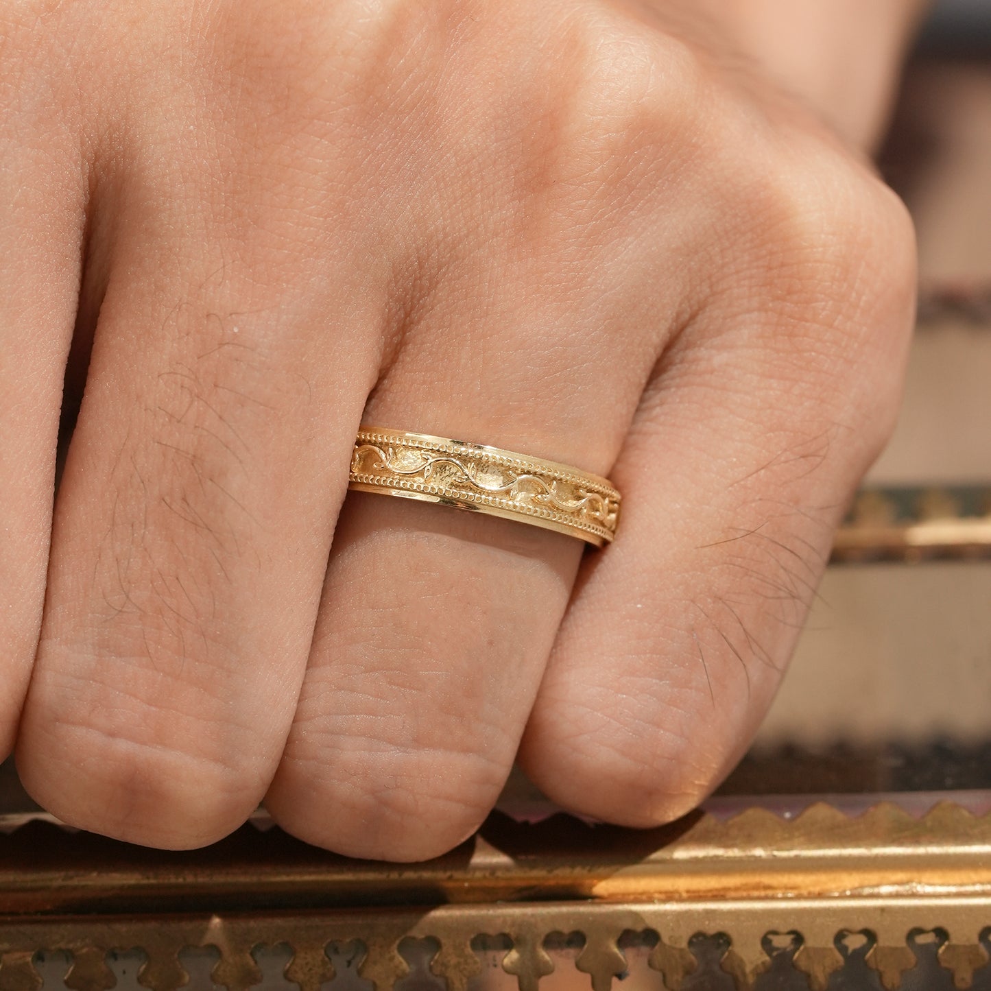 Detailed yellow gold men's band with vine engraving on hand