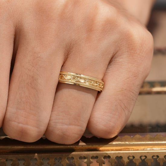 Detailed yellow gold men's band with vine engraving on hand
