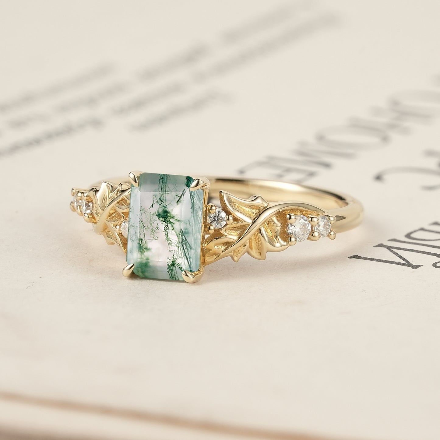 Moss agate ring with detailed leaves and diamonds showcased on an open book.