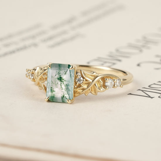 Moss agate ring with detailed leaves and diamonds showcased on an open book.