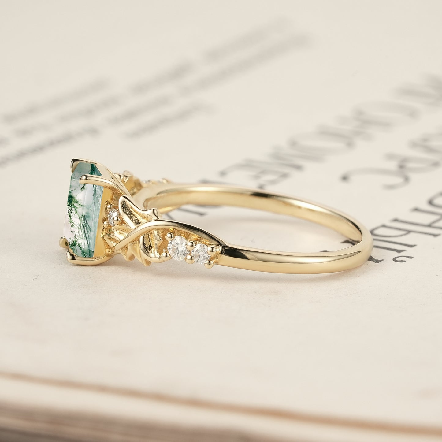 Nature-themed moss agate ring with gold band and round diamonds on an open book.