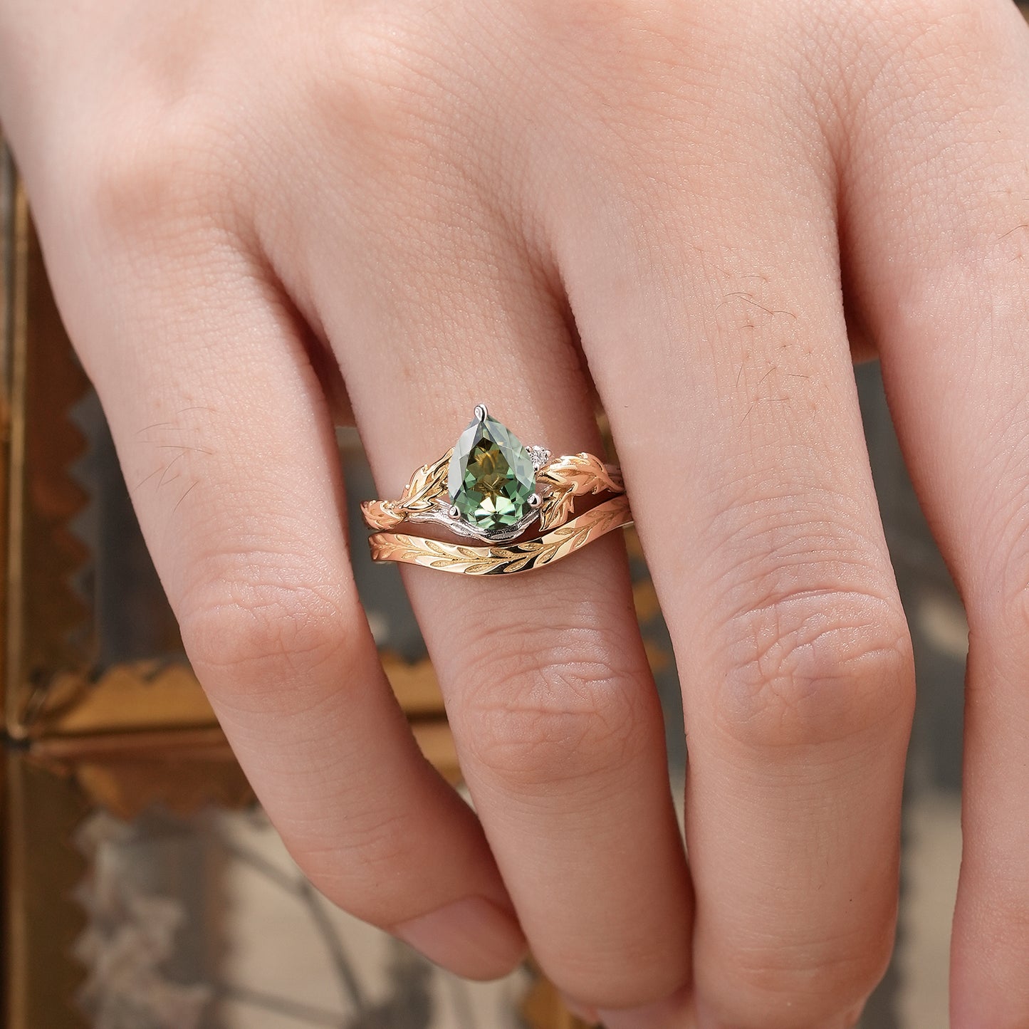 Leaf and wood pattern engagement ring set featuring pear-cut green sapphire.