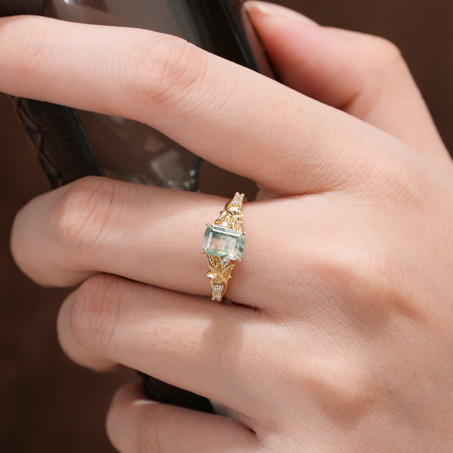 Emerald cut moss agate ring with gold band and sparkling diamonds on a woman's hand.