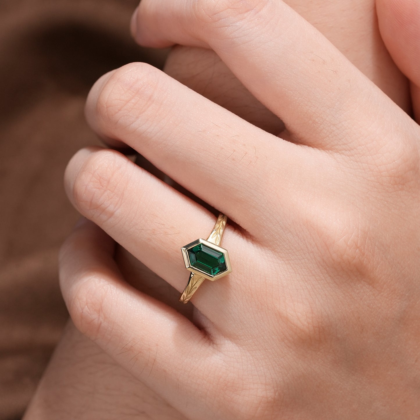 Elegant hexagon emerald ring on hand with nature-inspired gold band.