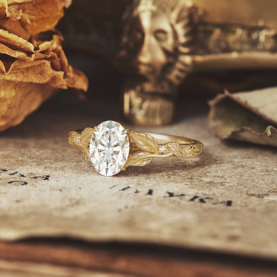 Nature-inspired oval moissanite ring in gold with intricate leaf design on vintage backdrop.