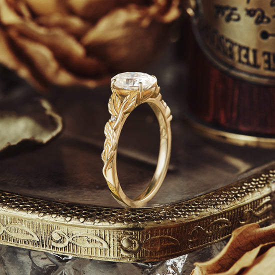 Elegant oval moissanite ring in gold with intricate leaf details on vintage tray.