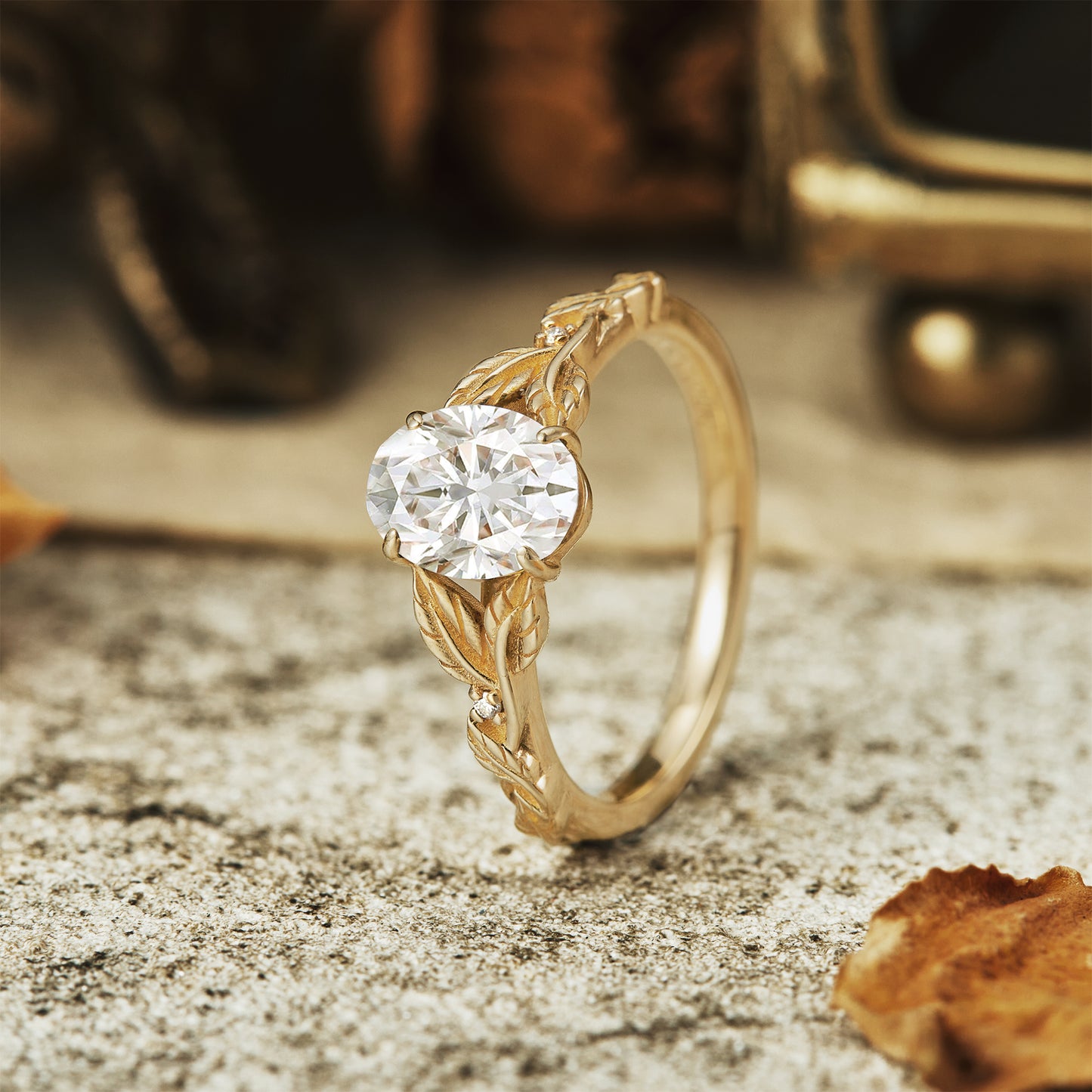 Moissanite oval ring in gold with detailed leaf design on vintage stone surface.