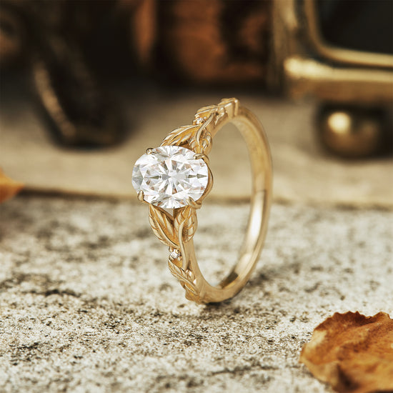 Moissanite oval ring in gold with detailed leaf design on vintage stone surface.
