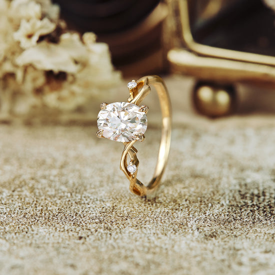 Floral engagement ring with oval moissanite and twisted gold band on textured surface
