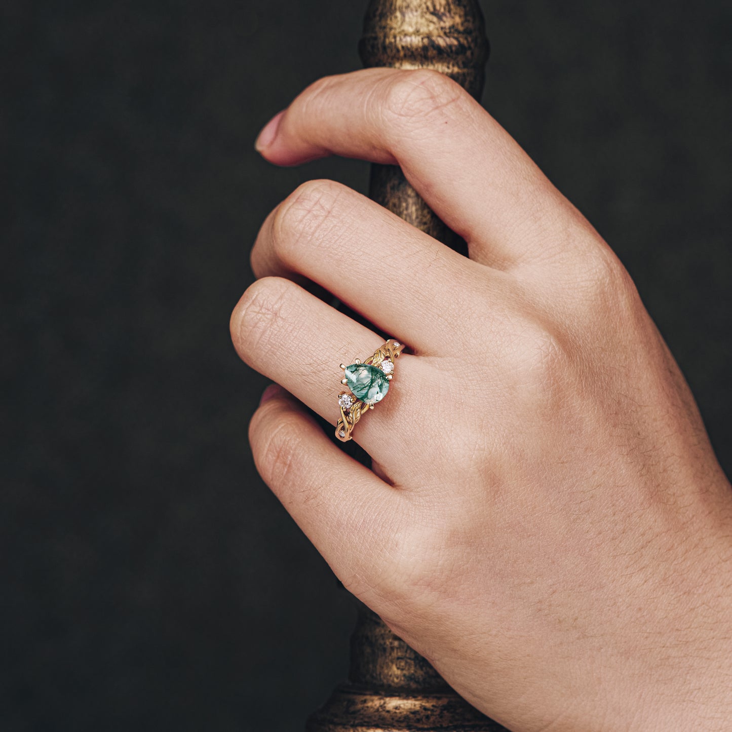 Moss agate pear cut ring with moissanite accents on a hand, unique gold design.