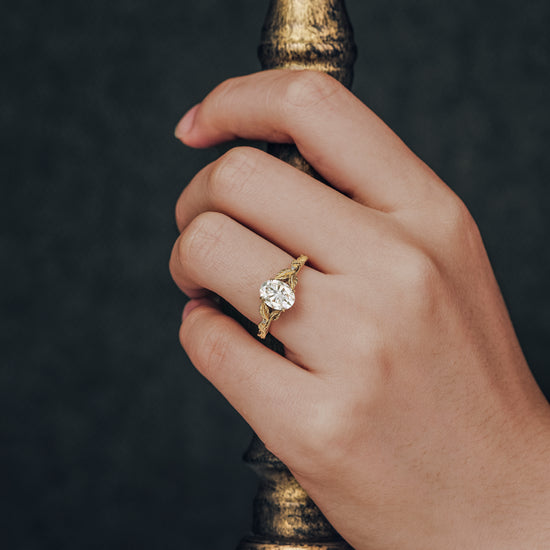 Hand wearing oval moissanite leaf ring in gold with nature-inspired details.