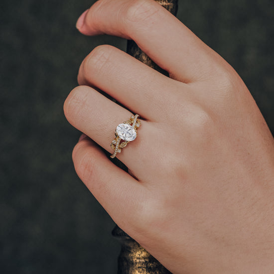 Moissanite engagement ring with oval cut and gold band featuring leaf accents.