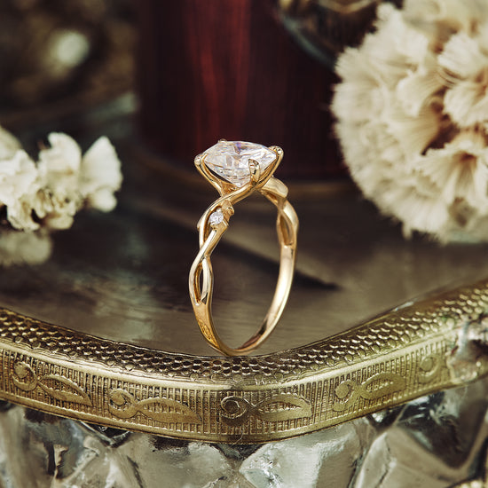 Twisted gold band engagement ring featuring central oval moissanite with floral design