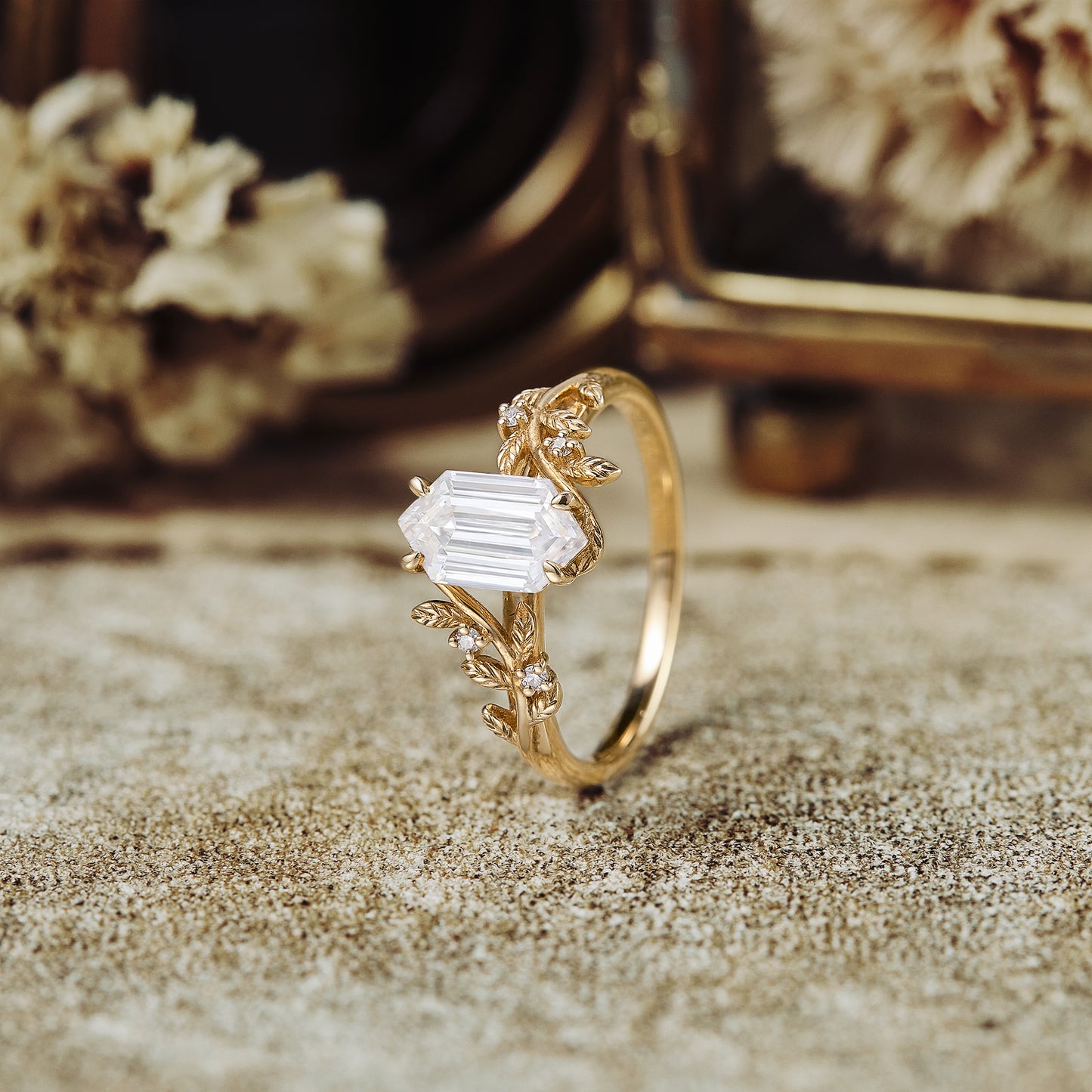 Leaf-inspired gold engagement ring with emerald-cut Moissanite, featuring floral details.