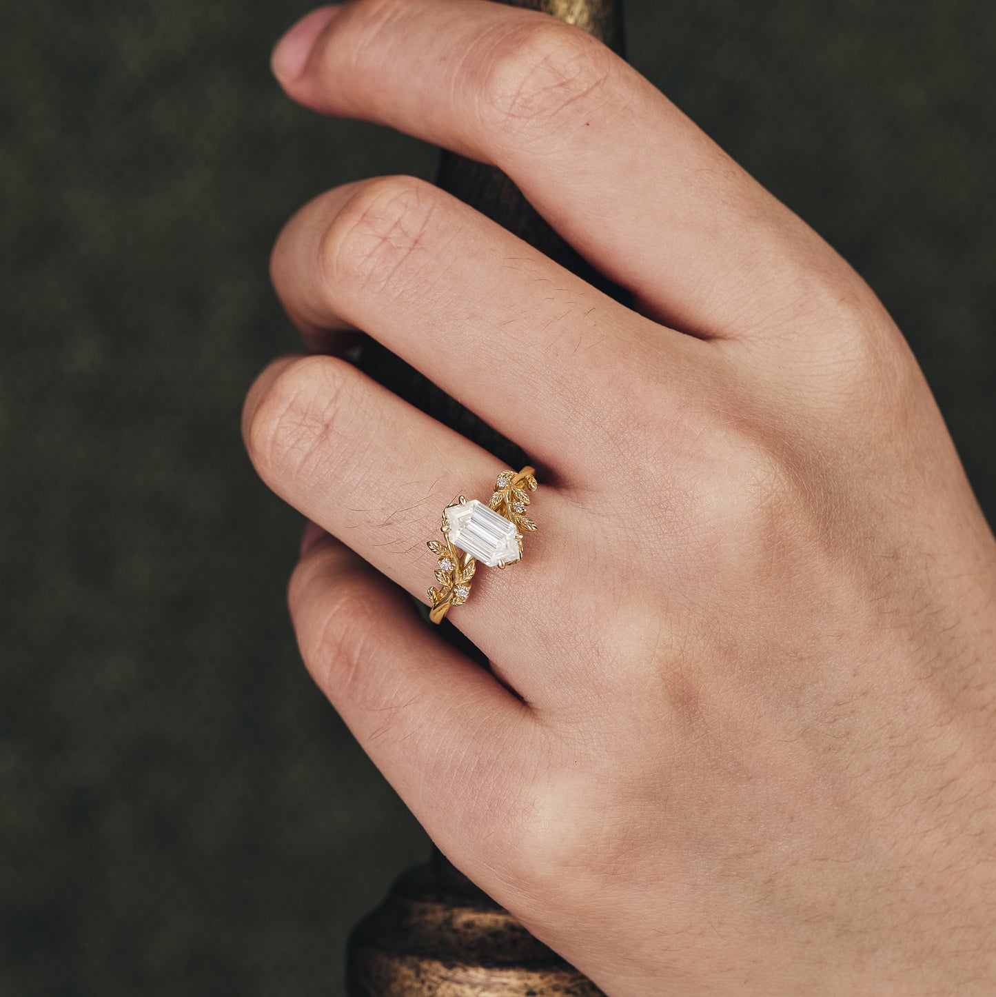 Leaf-accented engagement ring with emerald-cut Moissanite on hand.
