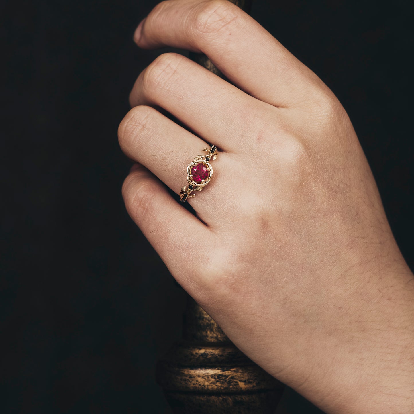 Delicate Blooming Rose ring with ruby, showcased on hand holding candlestick.