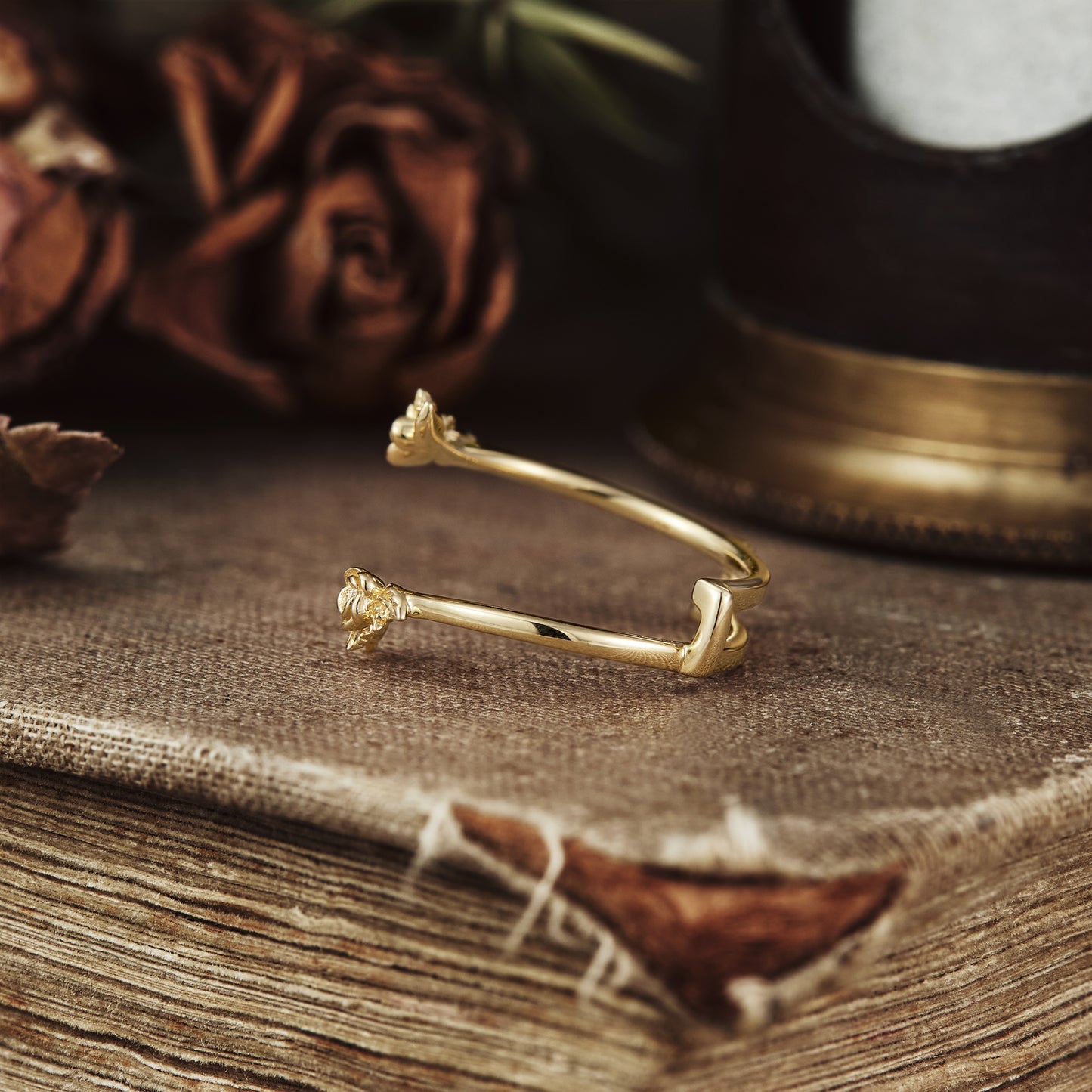 Nature-inspired gold wedding ring with floral motifs resting on a textured surface.