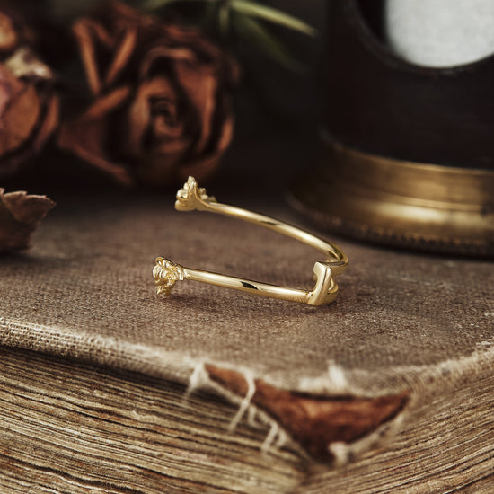 Nature-inspired gold wedding ring with floral motifs resting on a textured surface.