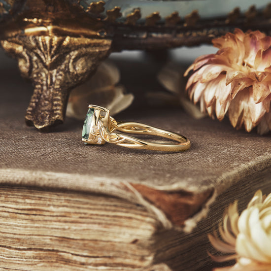 Cora pear cut green sapphire ring in gold next to flowers and vintage book