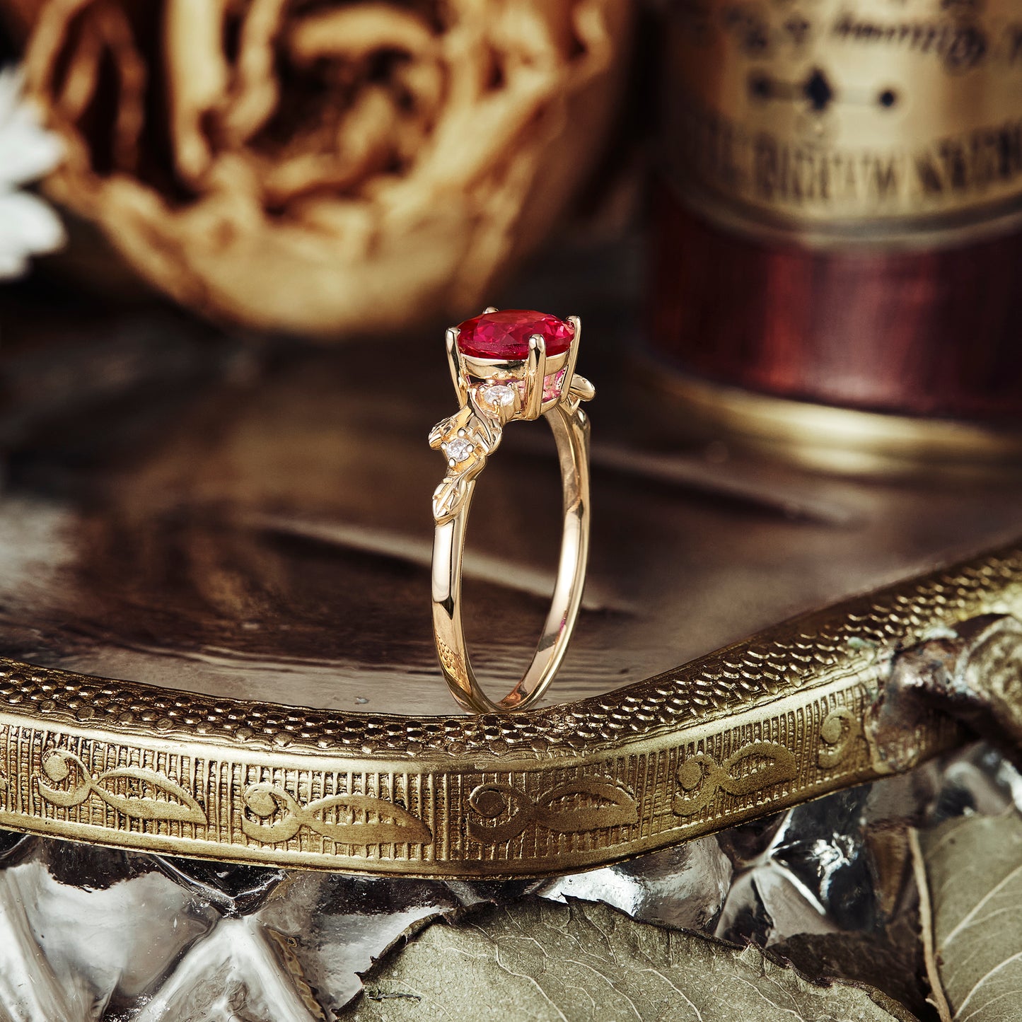 Nature-inspired ruby engagement ring with leaf details on a decorative metallic surface