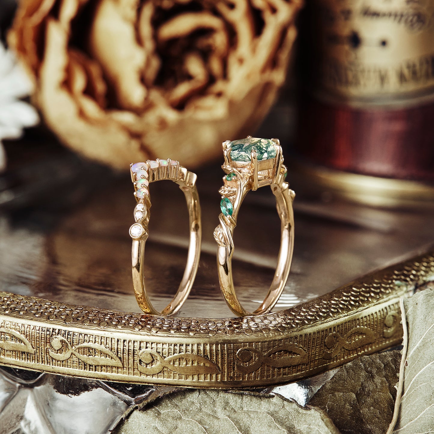 Moss agate ring with emerald accents on a vintage tray with a flower backdrop.