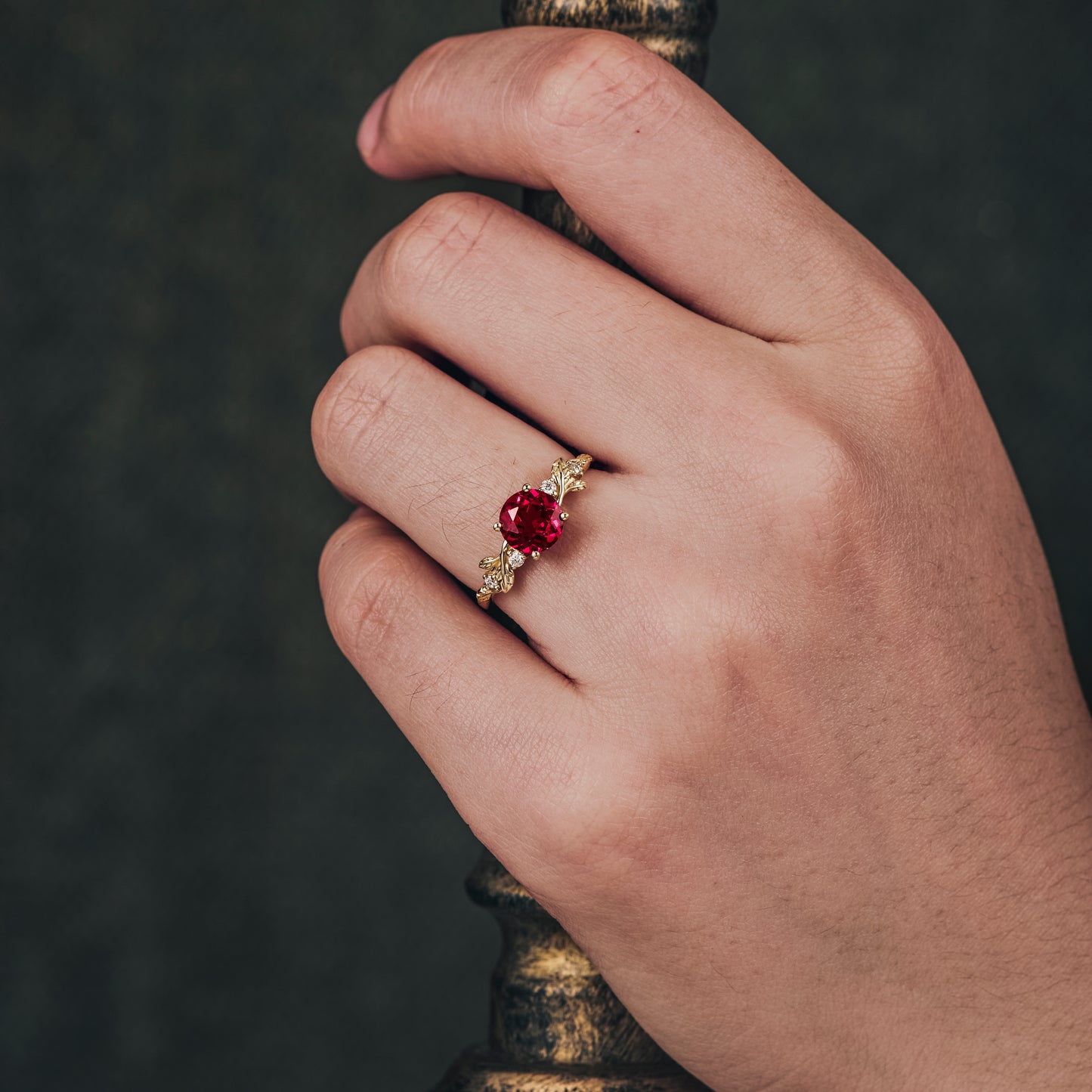 Hand displaying ruby engagement ring with moissanite side stones on gold band.