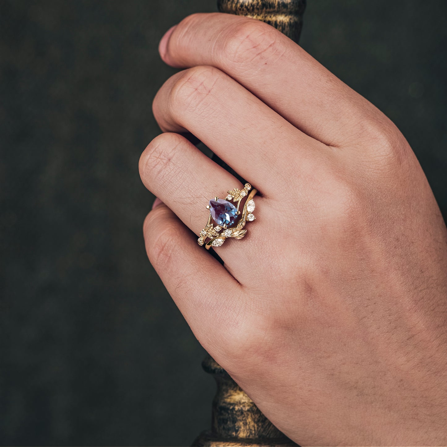 Hand wearing nature-inspired gold ring set with pear-cut alexandrite and diamonds.