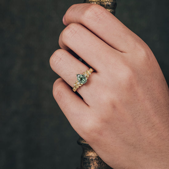Cora green sapphire pear cut ring on hand with floral gold design and moissanite accents.