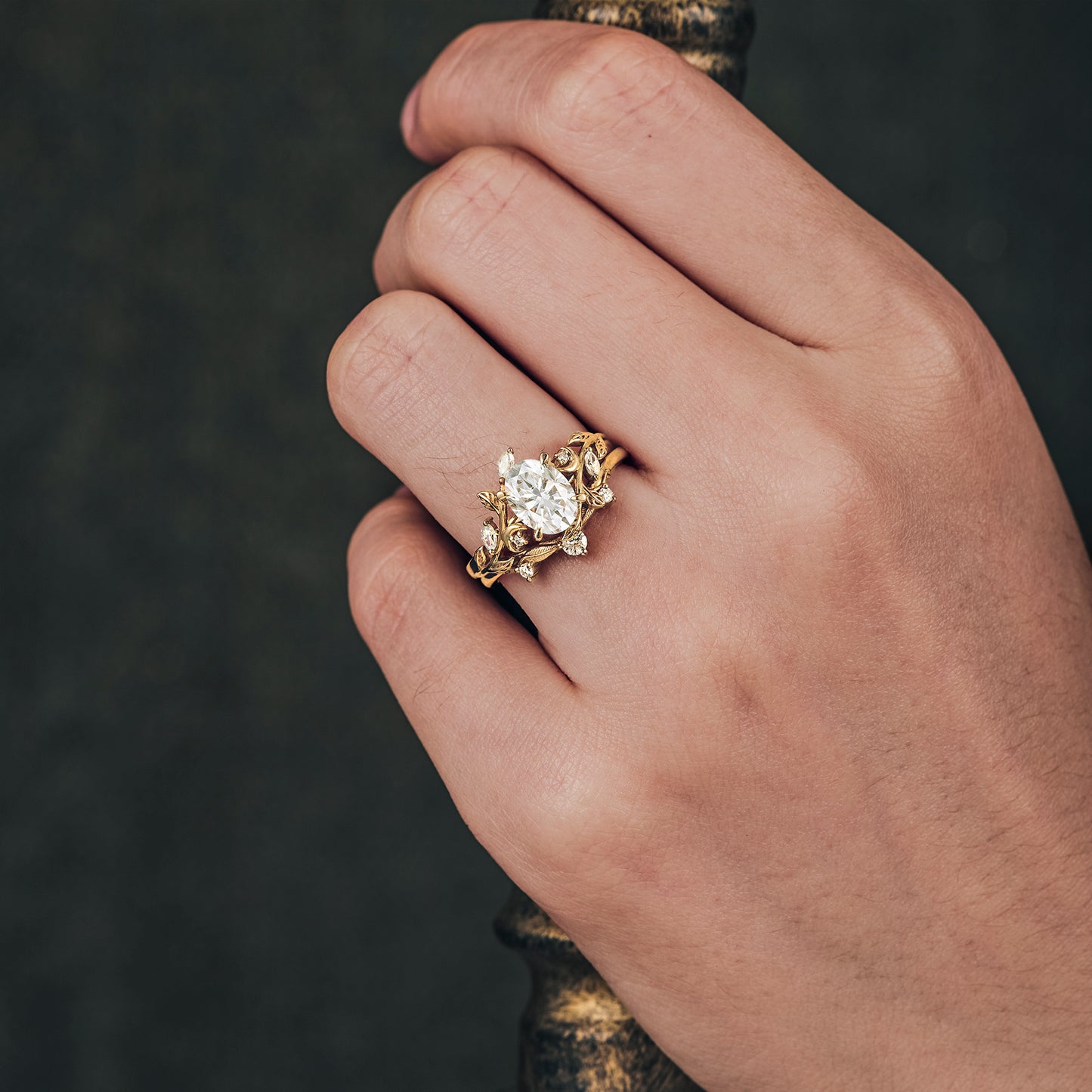 Leaf-inspired yellow gold ring with oval moissanite on a hand, showcasing floral design.