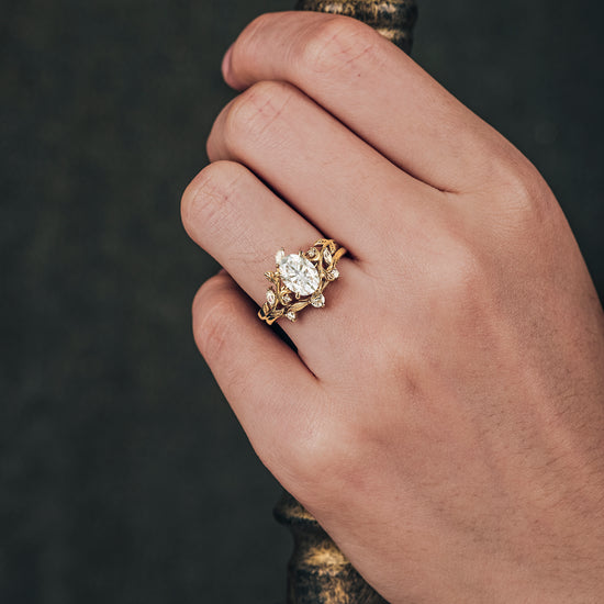 Leaf-inspired yellow gold ring with oval moissanite on a hand, showcasing floral design.
