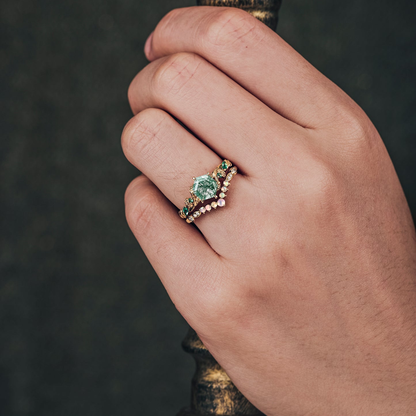 Hand wearing nature-inspired moss agate ring with emerald accents on gold band.