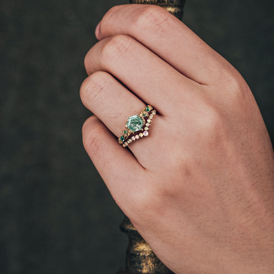 Hand wearing nature-inspired moss agate ring with emerald accents on gold band.