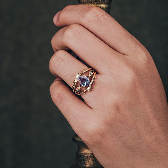 Leaf enhancer ring featuring pear-cut alexandrite and moissanite accents on gold band.