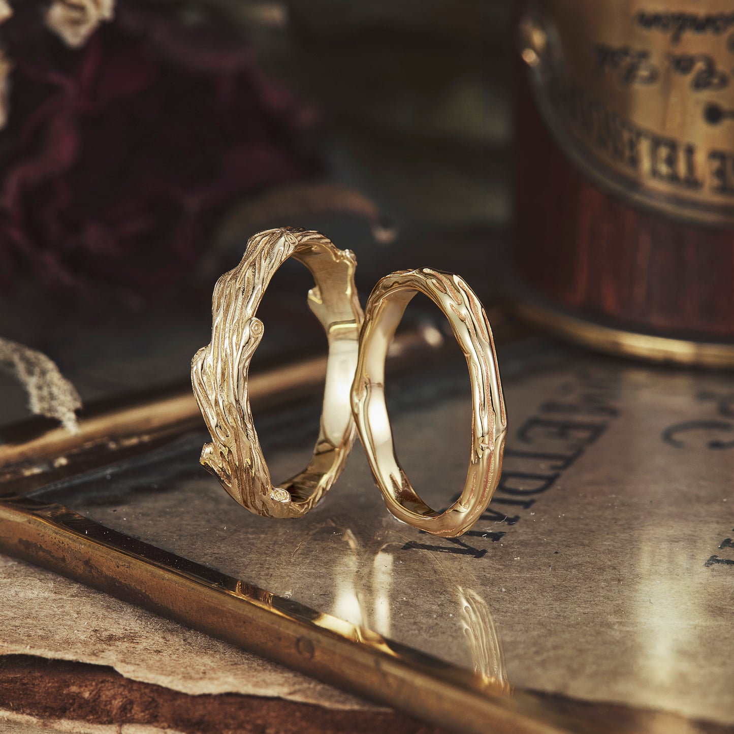 Solid gold couple rings with intricate tree branch design on elegant backdrop.