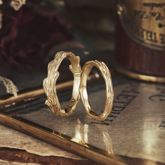Solid gold couple rings with intricate tree branch design on elegant backdrop.
