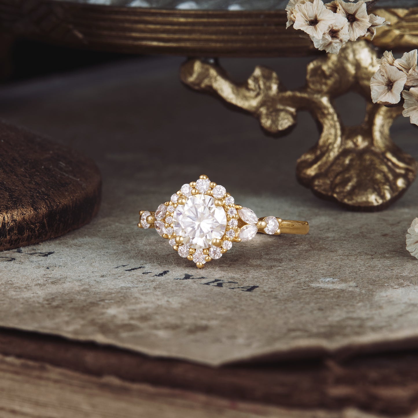 Moissanite halo ring with round stone, ornate gold band, on textured vintage surface.
