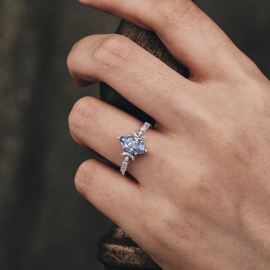 Hand wearing marquise gray moissanite engagement ring with round side stones.