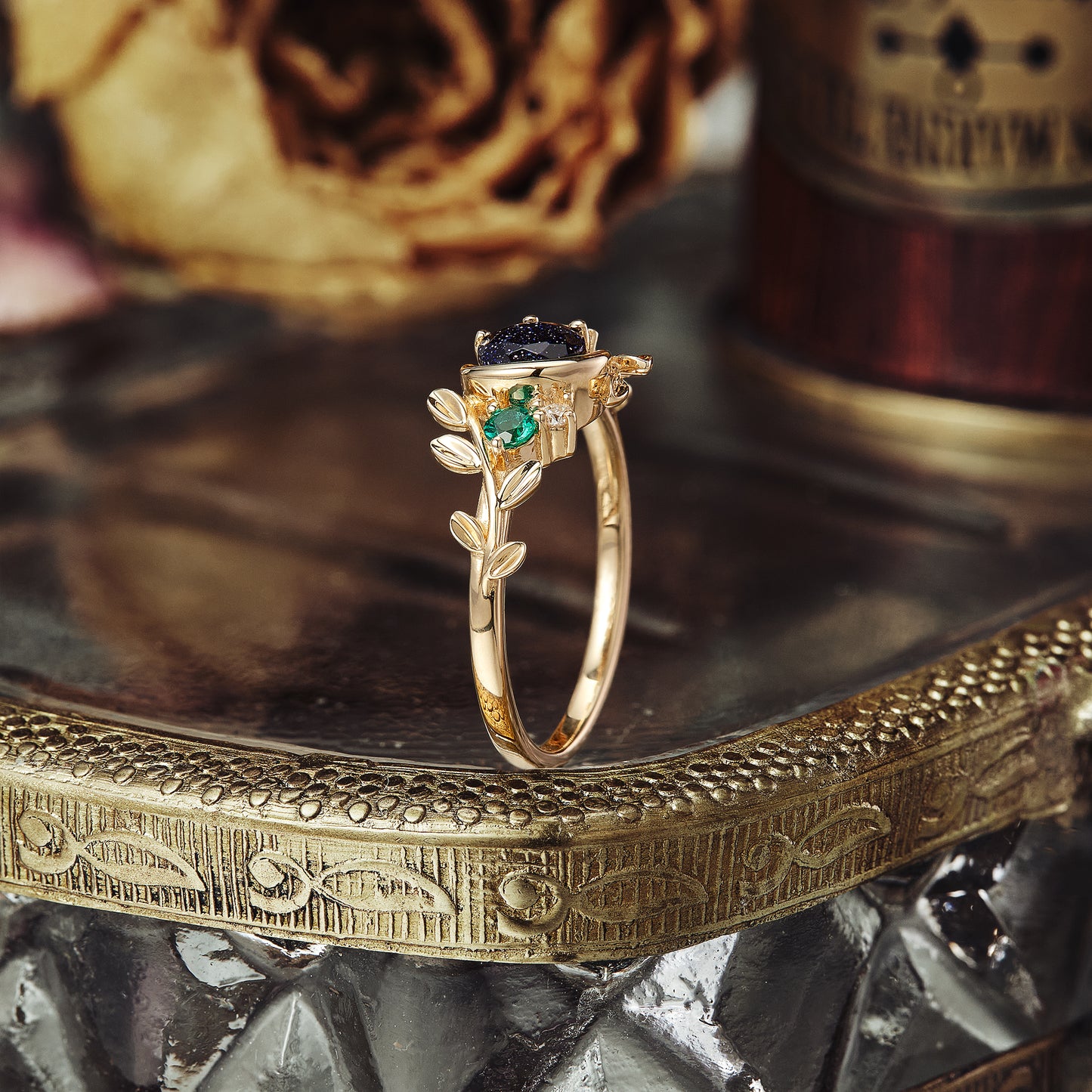 Gold ring featuring star sandstone, emerald, and nature-inspired leaf design.