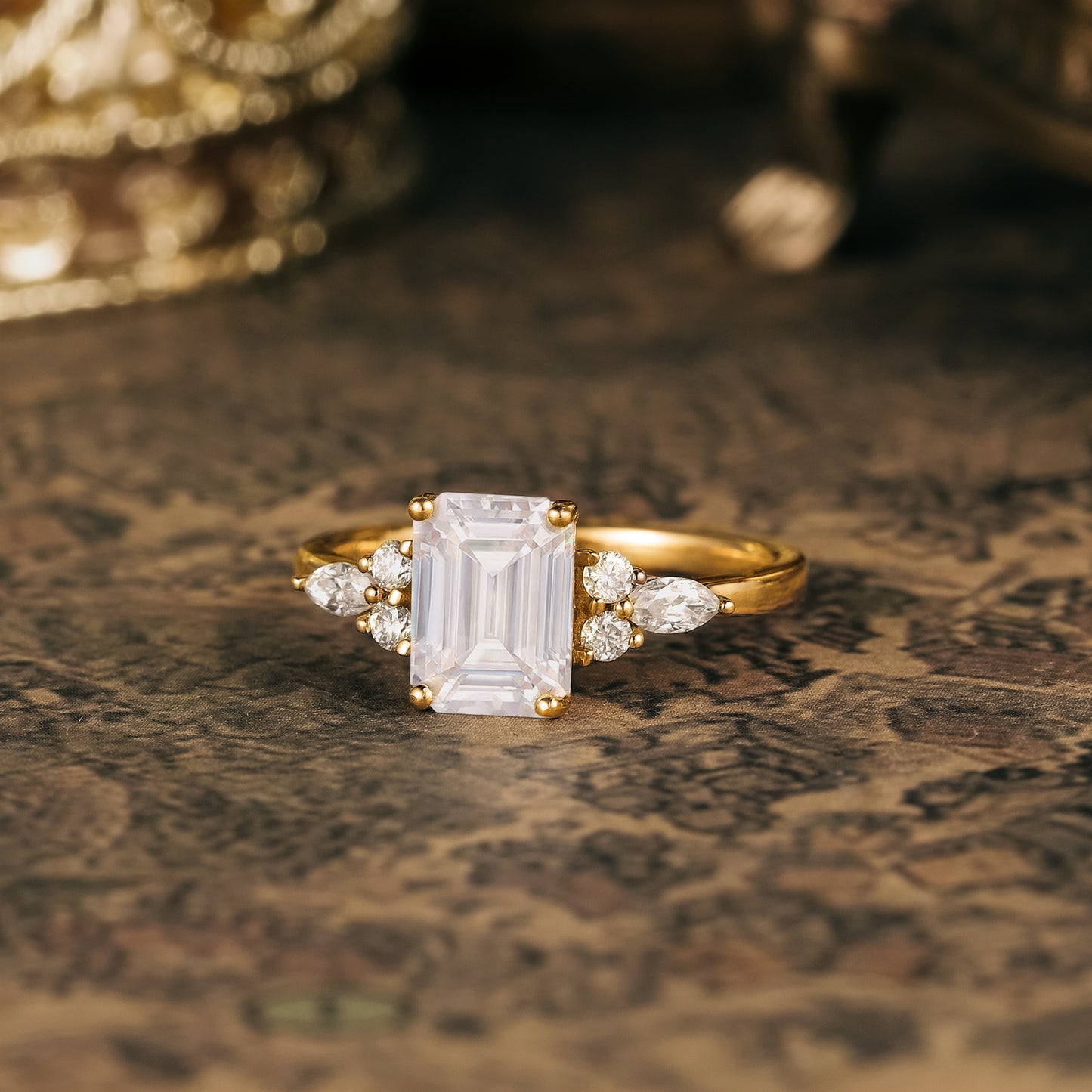 Emerald cut moissanite engagement ring with round and marquise side stones in gold.