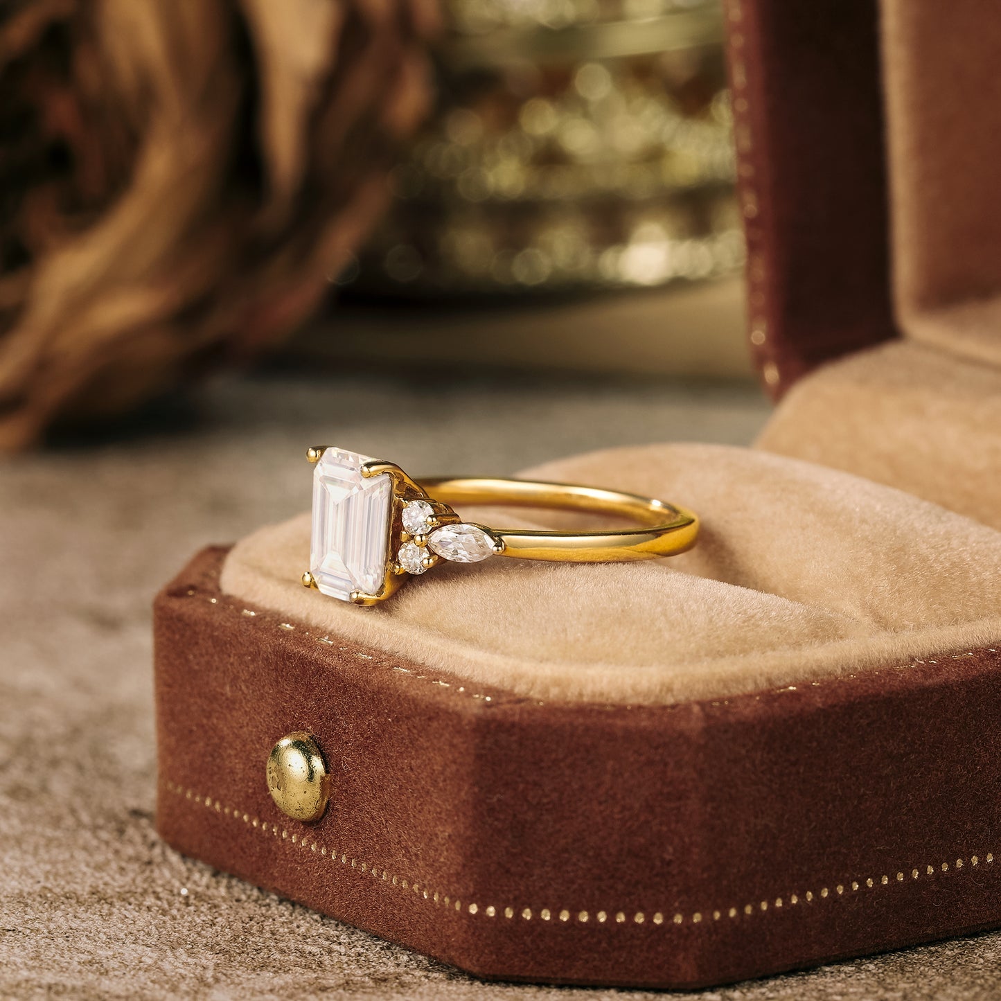 Emerald cut moissanite ring in gold with marquise side stones on velvet background.