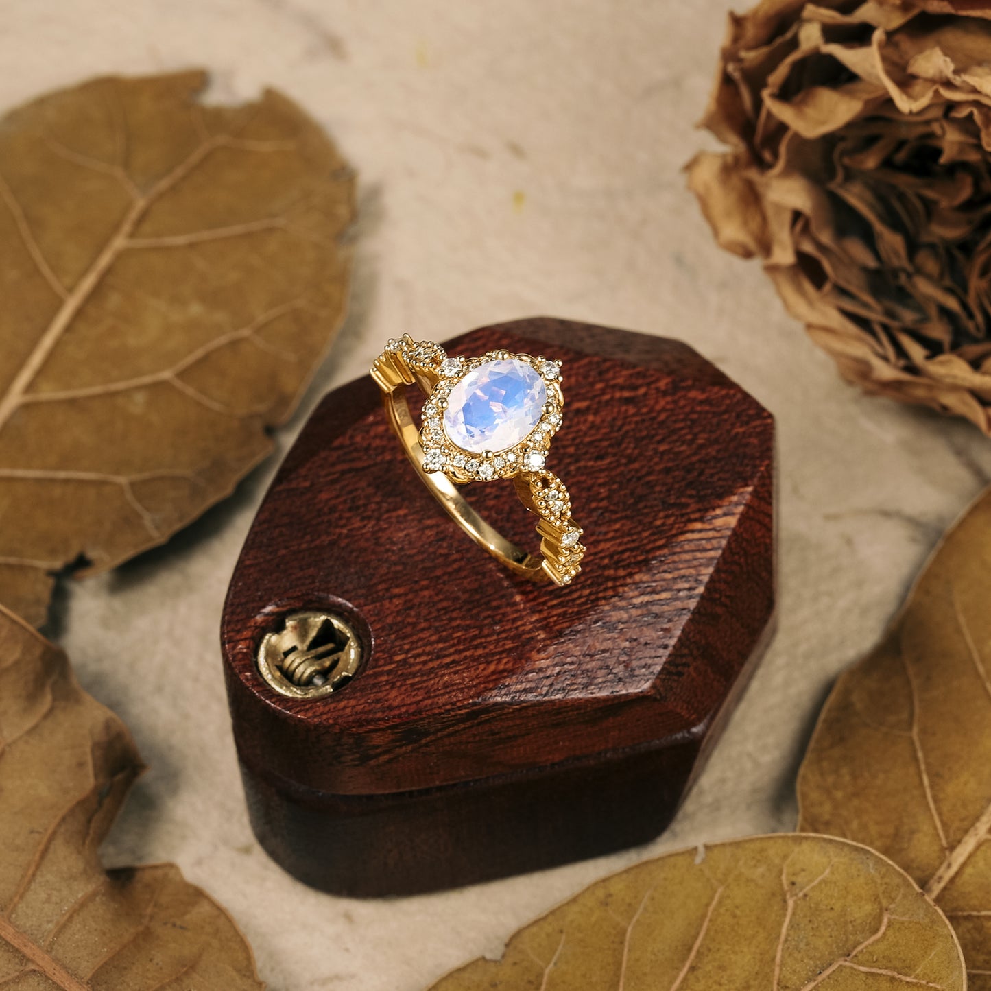 Gold Arabella moonstone halo engagement ring with moissanite accents on wooden box