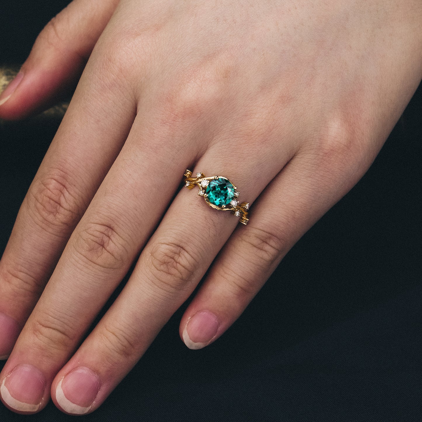 Teal gemstone ring on hand with twisted gold band, featuring nature-inspired details.