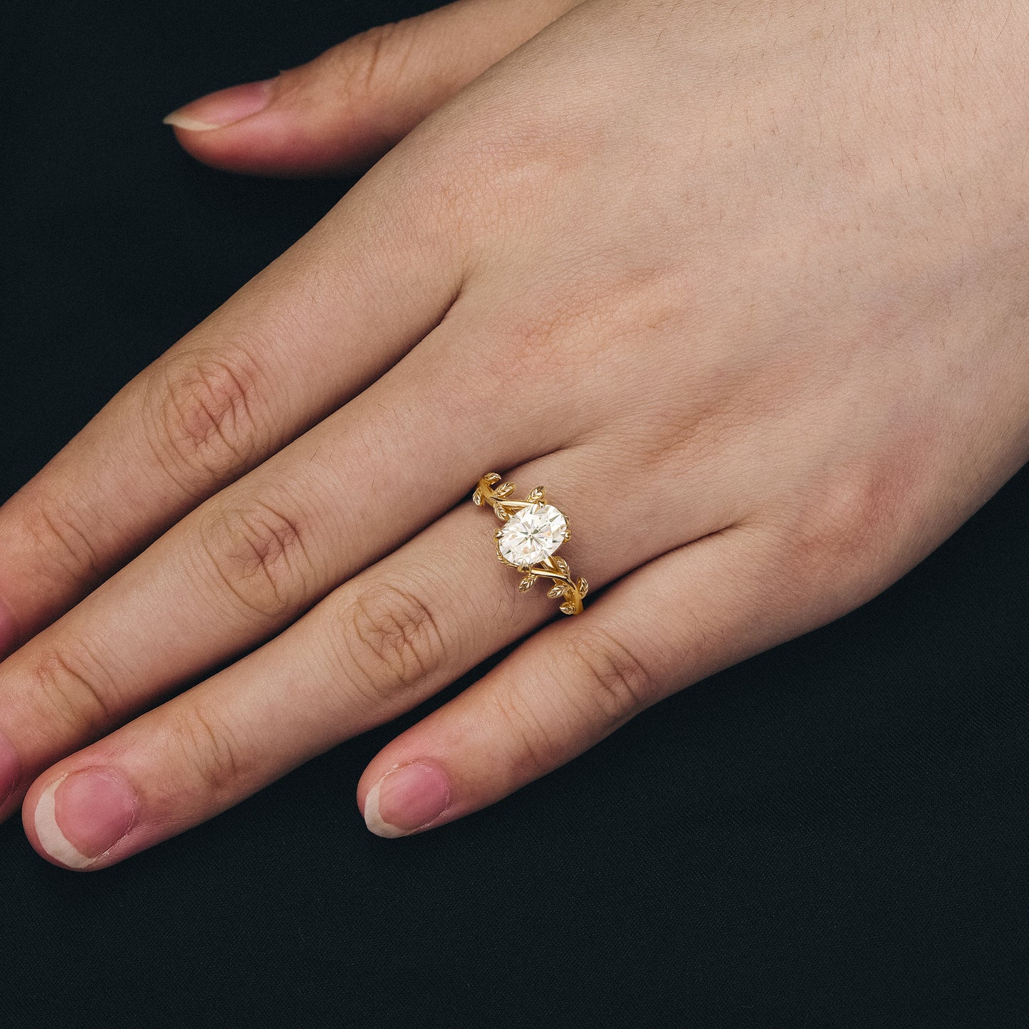 Gold engagement ring with oval moissanite and intricate leaf accents on band
