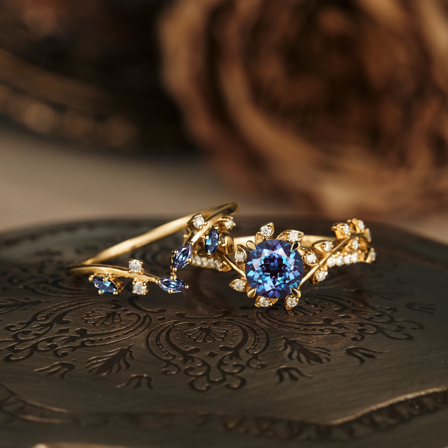 Blue gemstone and diamond leaf-inspired gold ring on decorative plate.