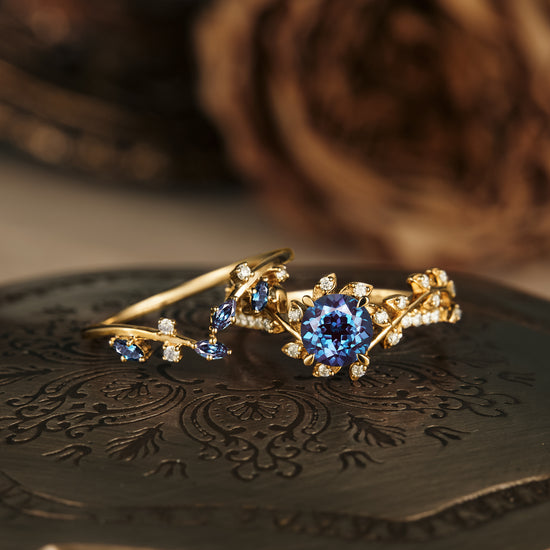 Blue gemstone and diamond leaf-inspired gold ring on decorative plate.