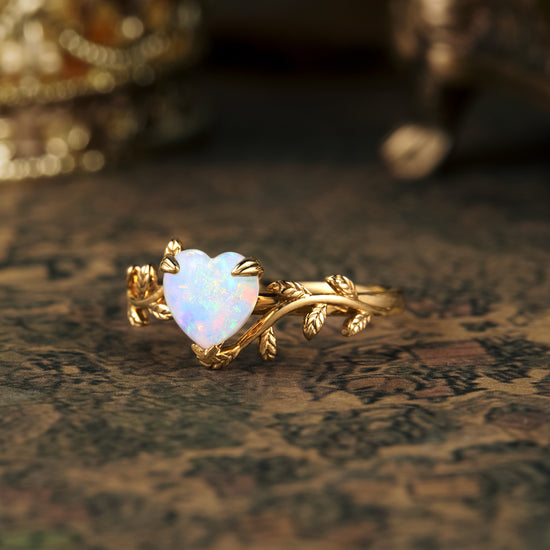 Heart-shaped opal ring with elegant gold leaves on a textured surface.