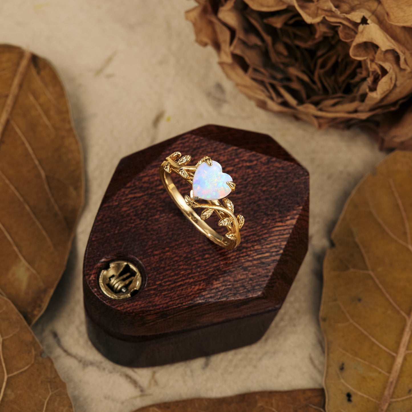 Nature-inspired gold heart opal ring with intricate leaf motif on wooden display.