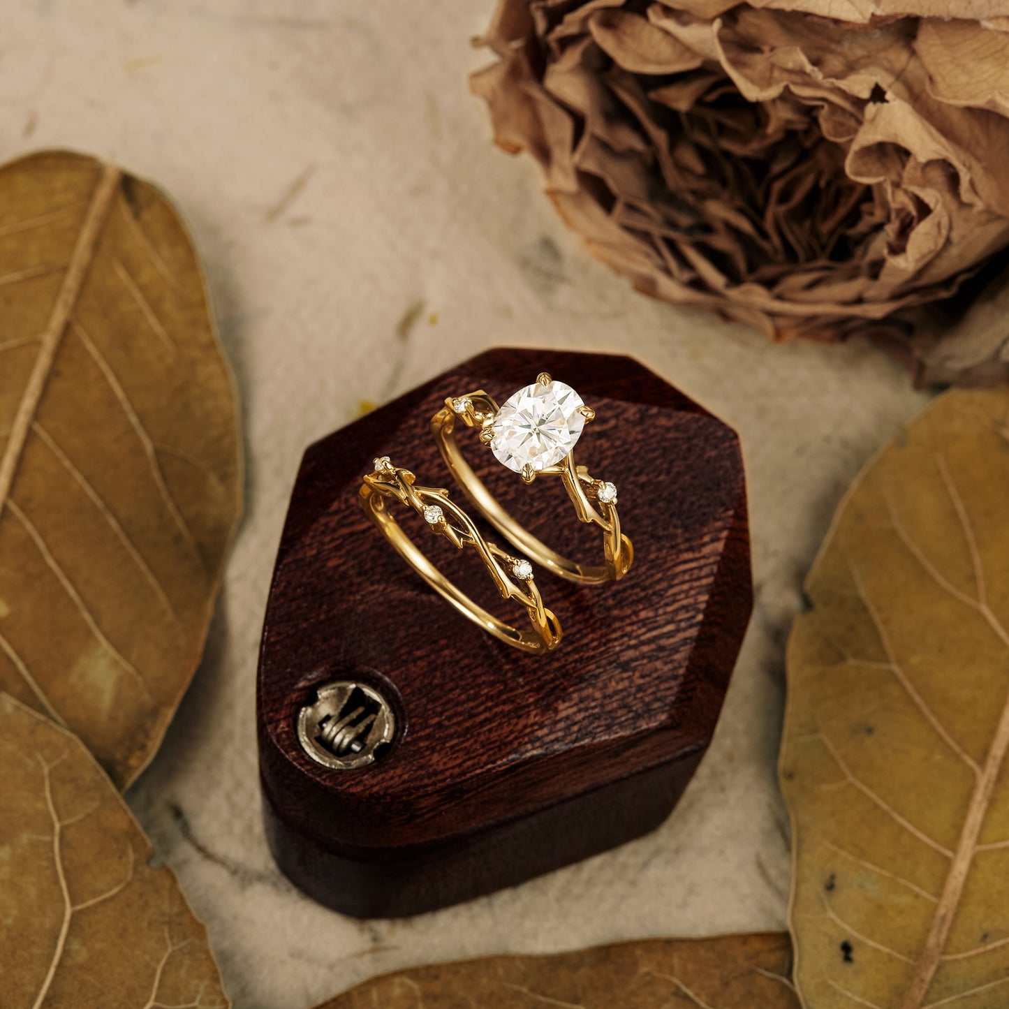 Oval moissanite floral engagement ring set on wooden display with leaves.